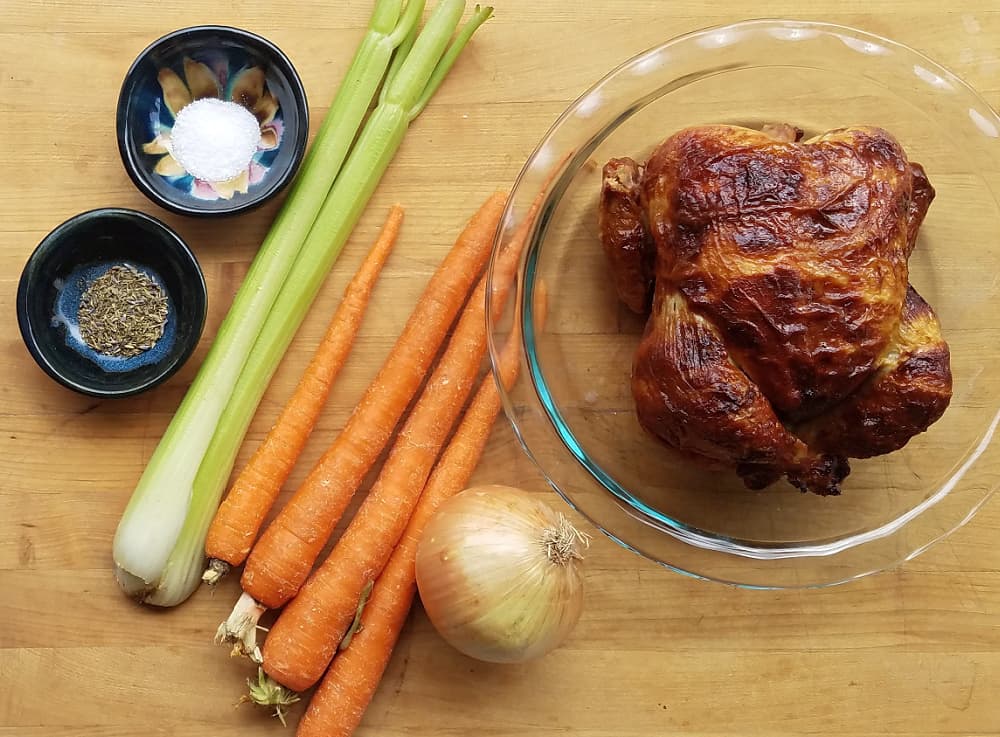 Celery, carrots, onion and rotisserie chicken on wooden cutting board. 