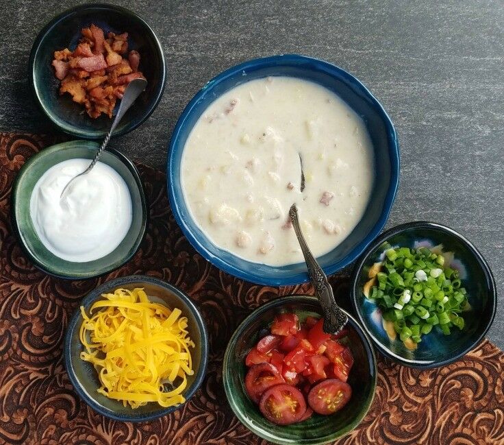 Bowl of cooked potato soup, with small bowls of topping ingredients surrounding it. 