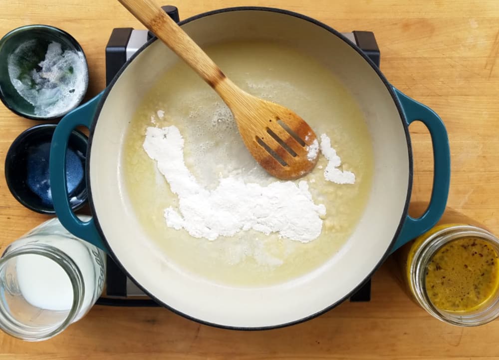 Flour and butter in skillet. Wooden spoon, empty ingredient bowls around. 