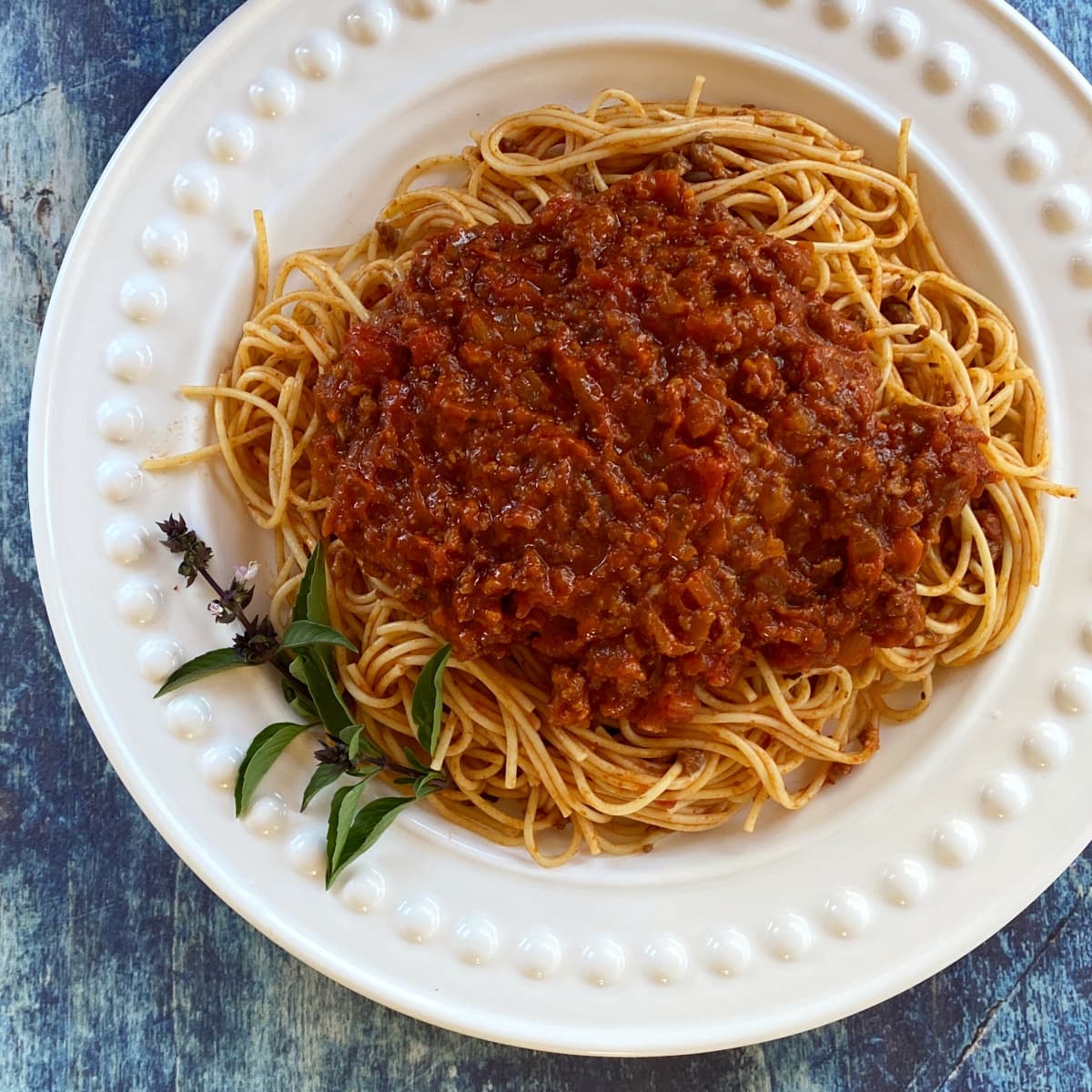 Meaty spaghetti sauce, served over thin spaghetti noodles on a large white plate.