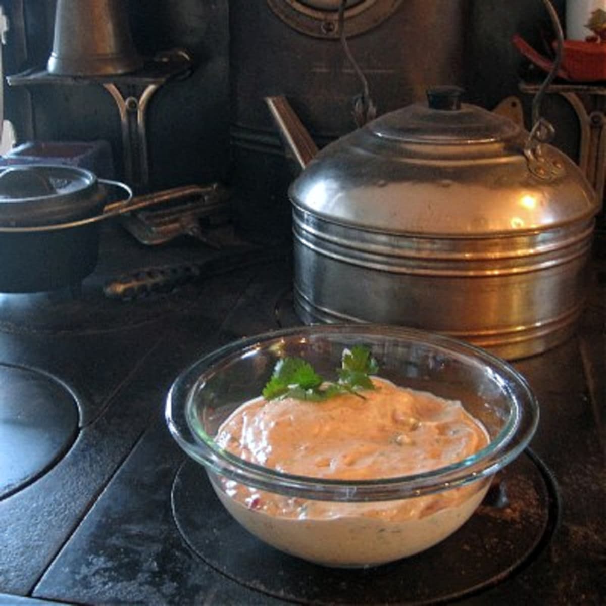 Bowl of creamy sauce in a glass bowl, resting in front of an antique tea kettle. 