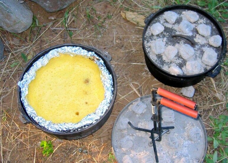 Two Dutch ovens, one with coals on top, and one with lid off, cake baked inside. Lid lifted on removed lid. 