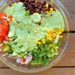 Closeup of cilantro dressing poured over ummer salad of beans, cilantro, pasta, onions, tomatoes, and corn.