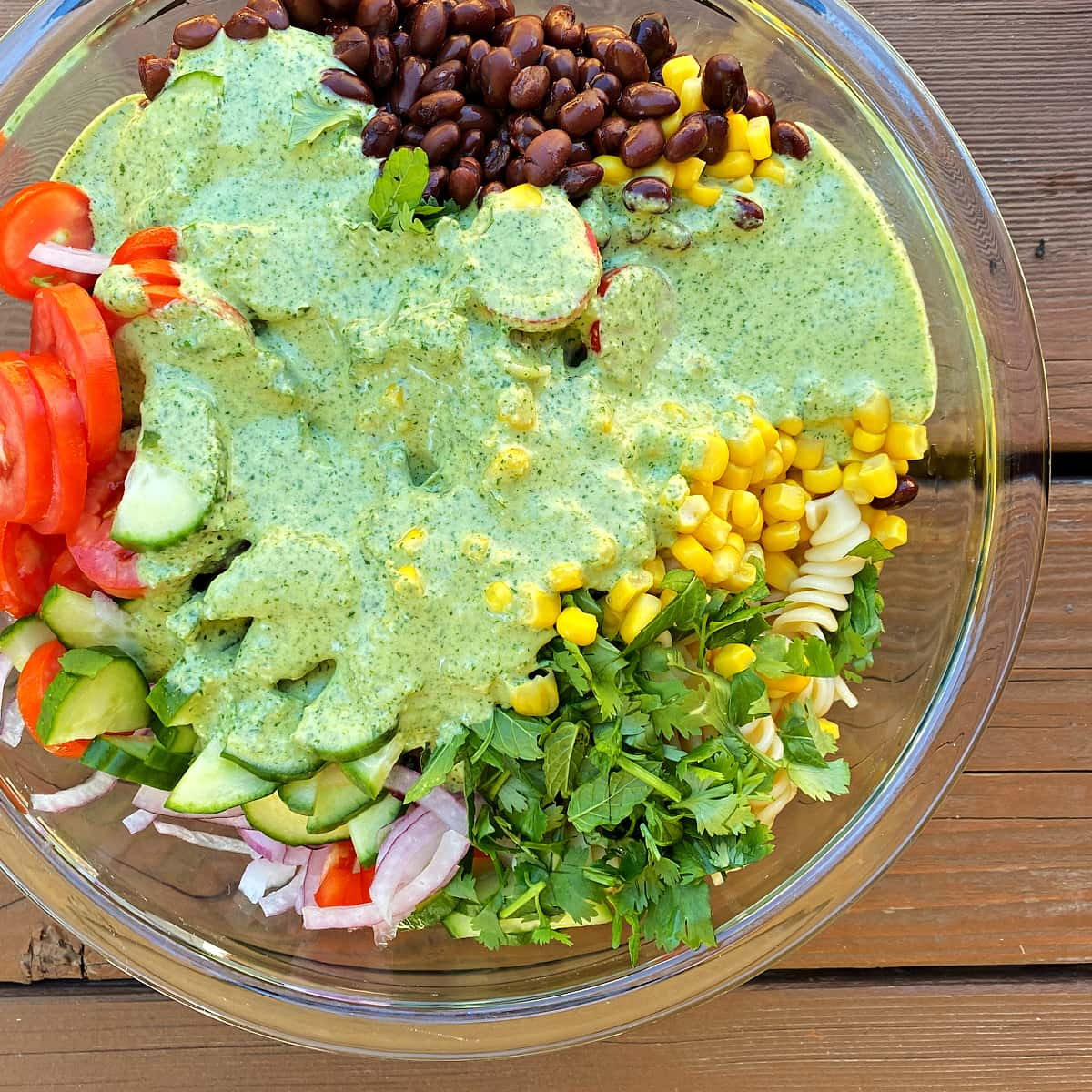 Closeup of cilantro dressing poured over ummer salad of beans, cilantro, pasta, onions, tomatoes, and corn.