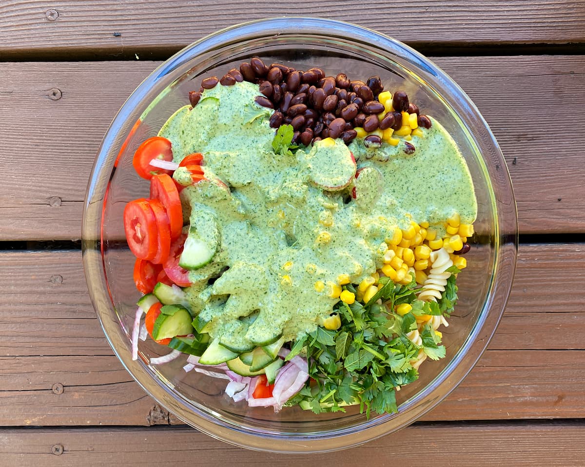 Summer salad of beans, cilantro, pasta, onions, tomatoes, corn, dressed with cilantro dressing and ready to mix.