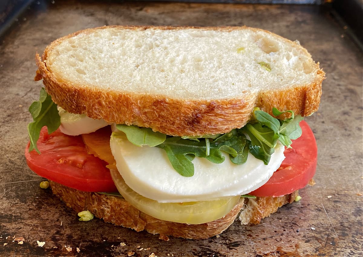 Closeup shot of an assembled sandwich with tomatoes, mozzarella, arugula, basil, etc., ready to eat, wrap, or grill.