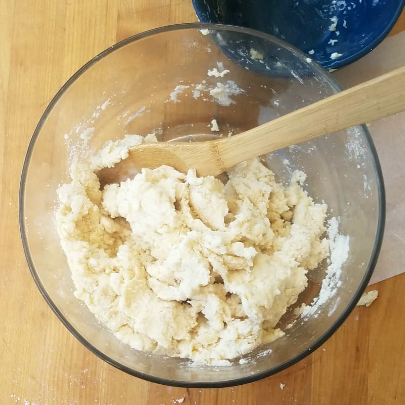 Ice water added to pie dough, being mixed with a wooden spoon. 