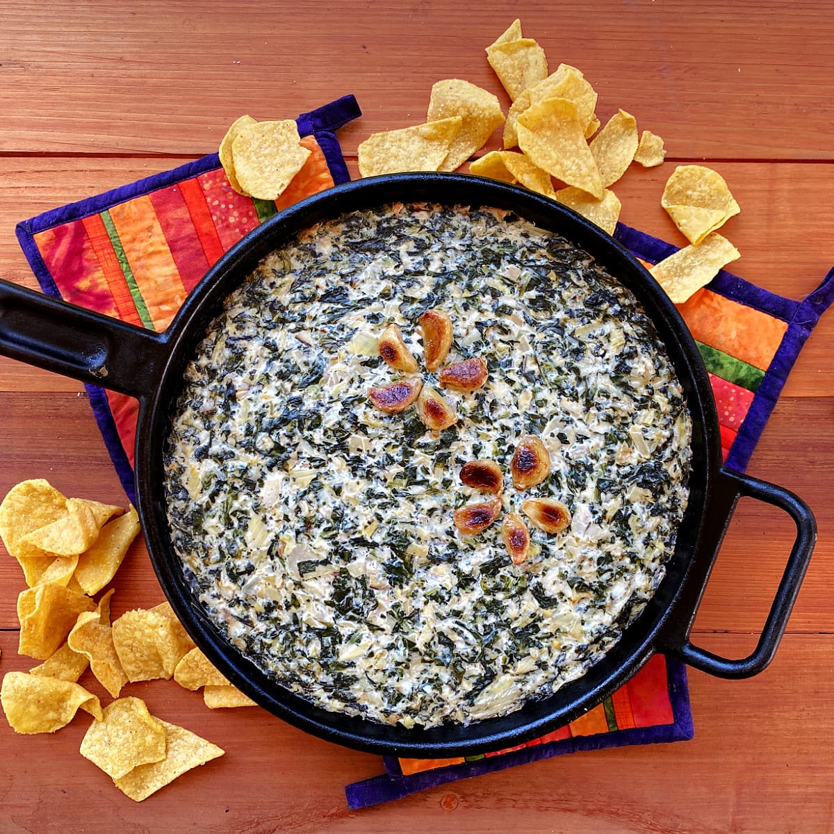 Overhead shot of spinach artichoke dip baked in a large cast iron skillet, with corn chips strewn at base. 
