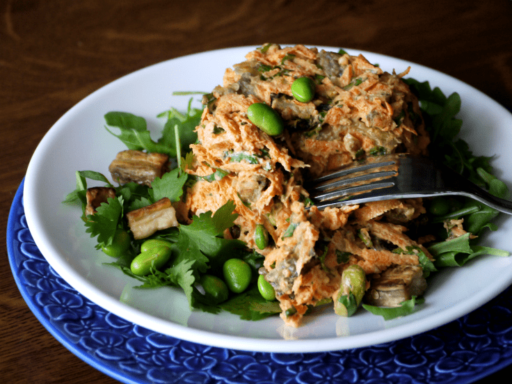 Salad made of grated carrots, edamame, and other ingredients on a white plate, garnished with cilantro. Fork in salad.  