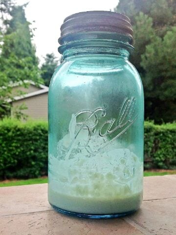 Old-sea-green Mason jar with a small amount of sourdough at the bottom.