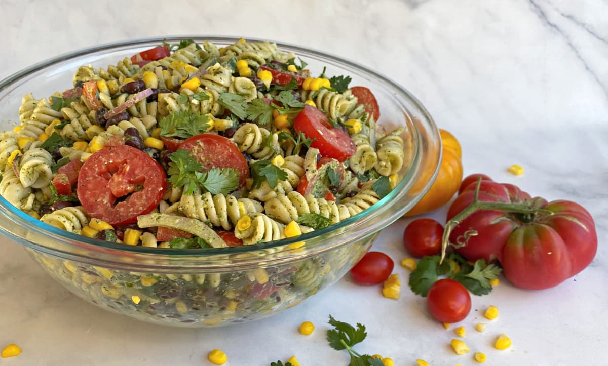 Prepared pasta salad in a glass serving bowl. Corn and tomatoes in foreground.