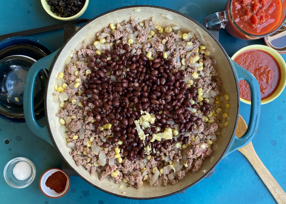 Black beans being added to skillet containing browned ground beef, onions, and corn. 