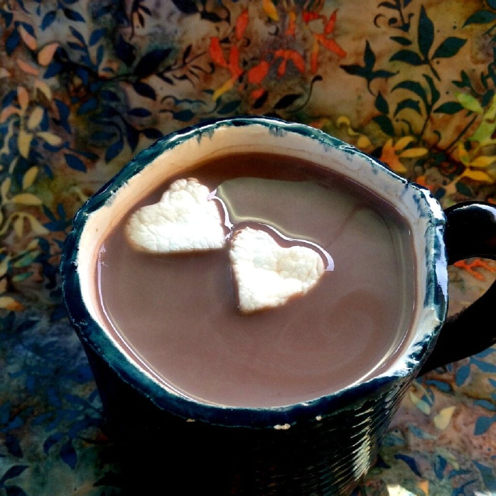 overhead shot of a cup of hot cocoa, with two heart-shaped marshmallows floating on top.