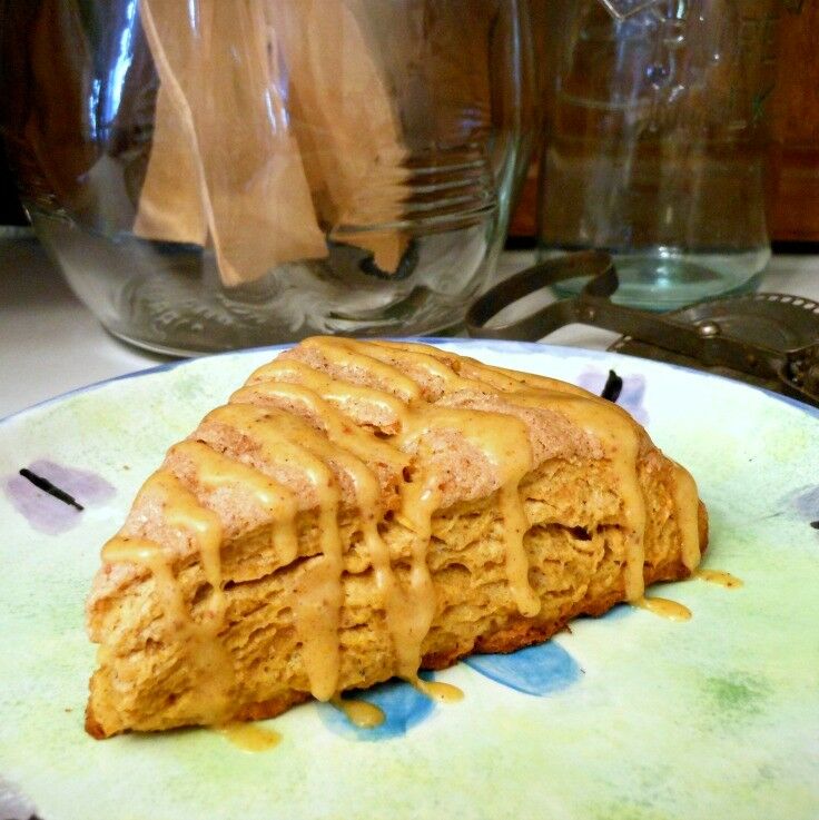 One scone on a plate, with old kithen implements in the background. 