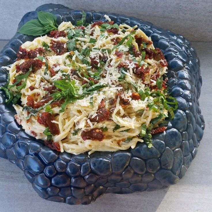 Pasta tossed with sun-dried tomatoes, parmesan, garnished with fresh basil, served on a highly textured bowl. 