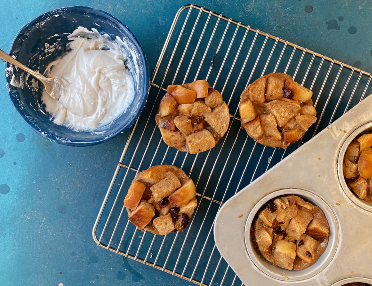 Baked bread pudding muffins on cooling rack. Frosting to the side.