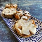 Four bread pudding muffins on a small, rectangular serving tray. Two are frosted, and two are dusted with powdered sugar.