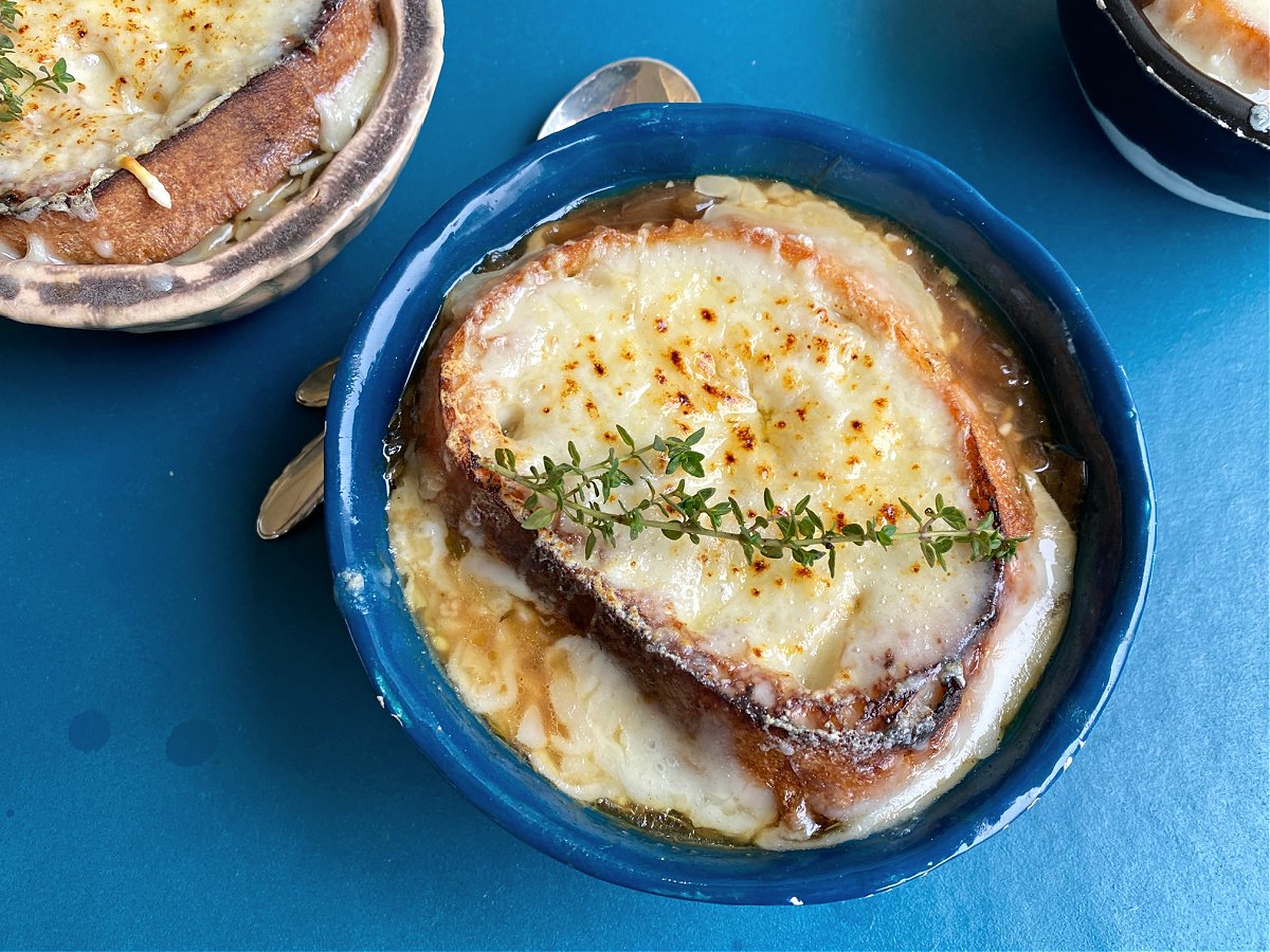 Classic French Onion Soup in a bowl. A sprig of time lays across the top. 