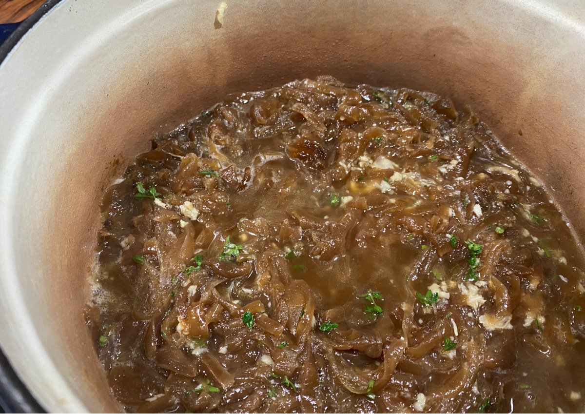 Soup stock with caramelized onions in pot. Fresh thyme floats on top. 