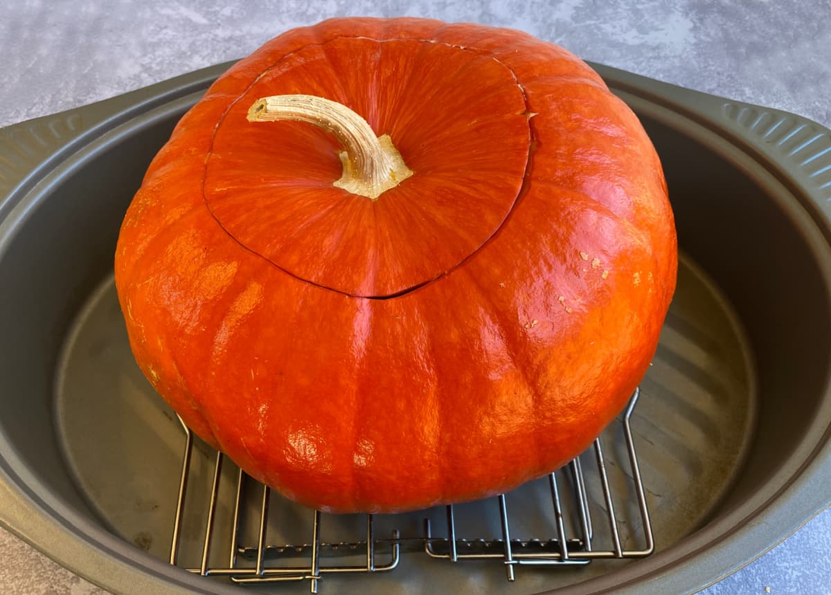 Stuffed, uncooked pumpkin with lid on, sitting in roasting pan.