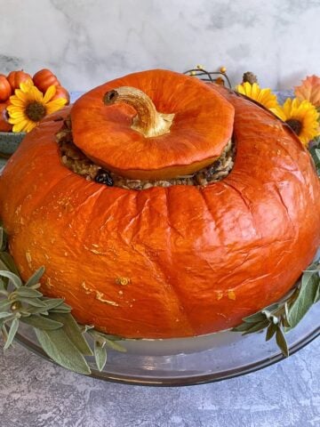 Whole stuffed pumpkin on glass stand, surrounded by fresh sage.