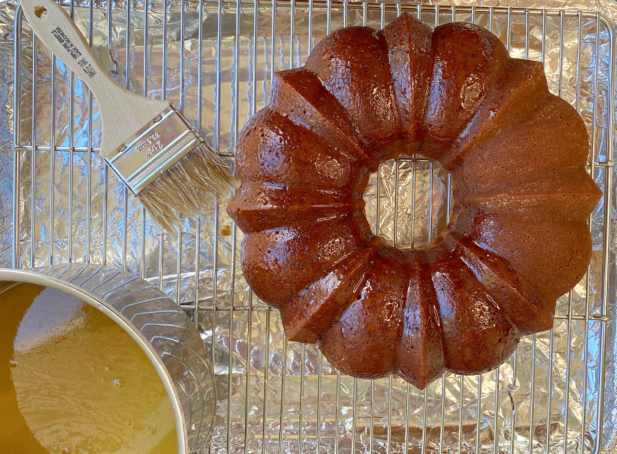 Baked bundt cake on cooling rack, with pastry brush and glaze to the side. 