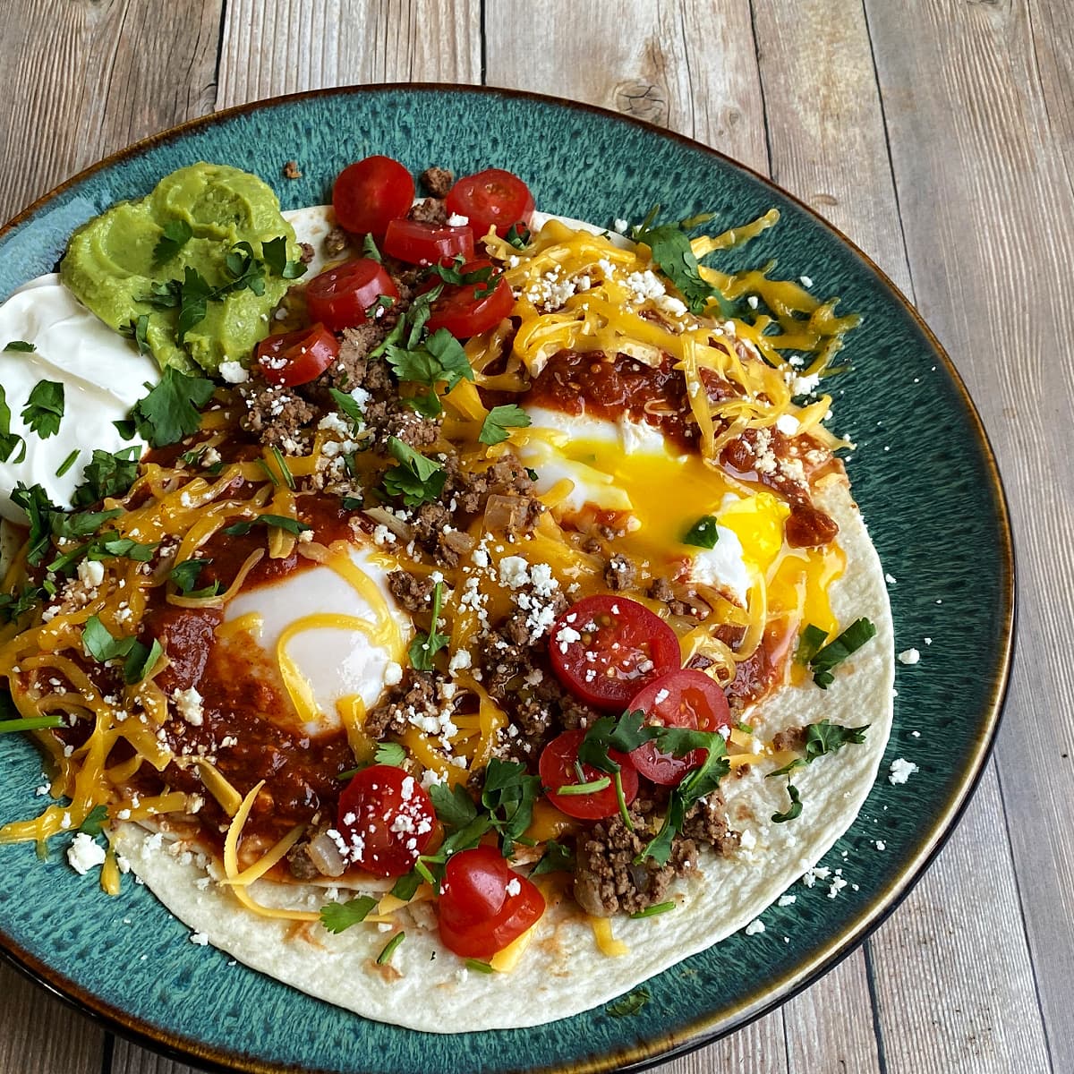Huevos rancheros, plated and topped with cheese, chorizo, beans, chopped cilantro.