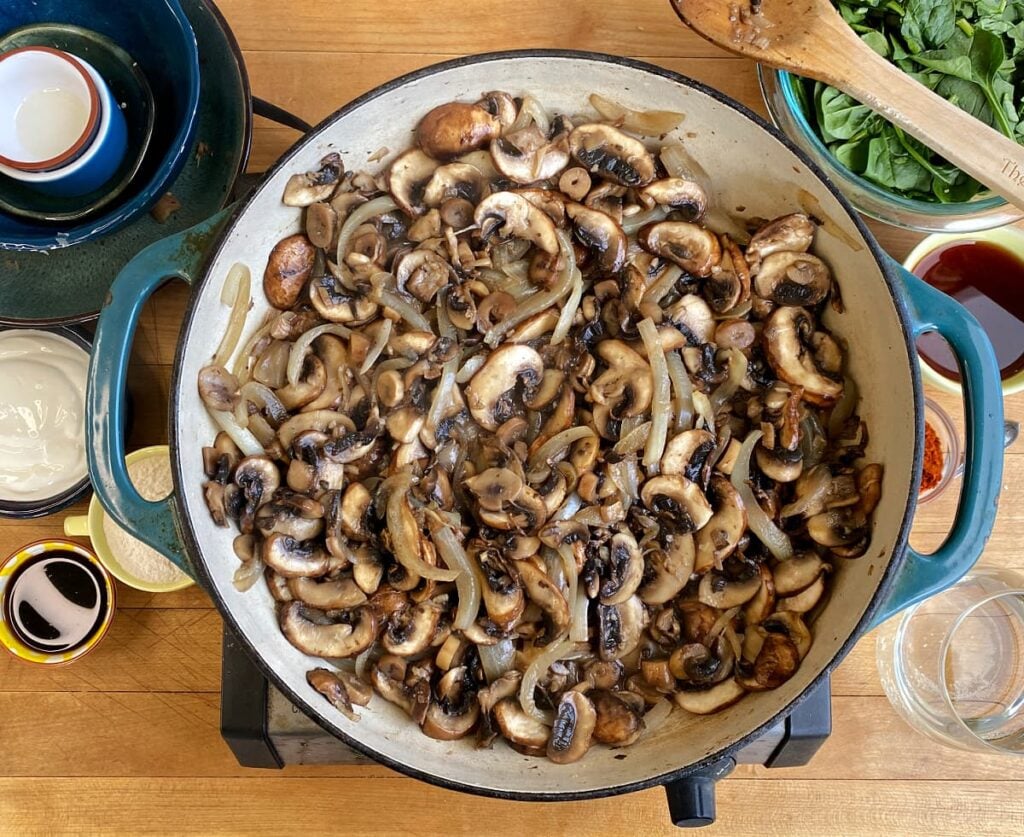 Mushrooms and onions cooking in a large enameled skillet.