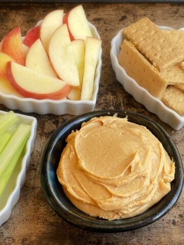 Small bowl of peanut butter dip, with other dippers in heart-shaped bowls around it.