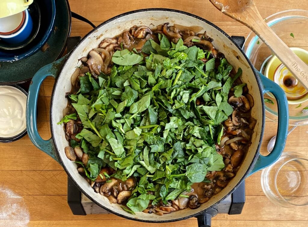 Chopped fresh spinach added to stroganoff mixture in skillet. Not mixed in yet - just sitting on top.