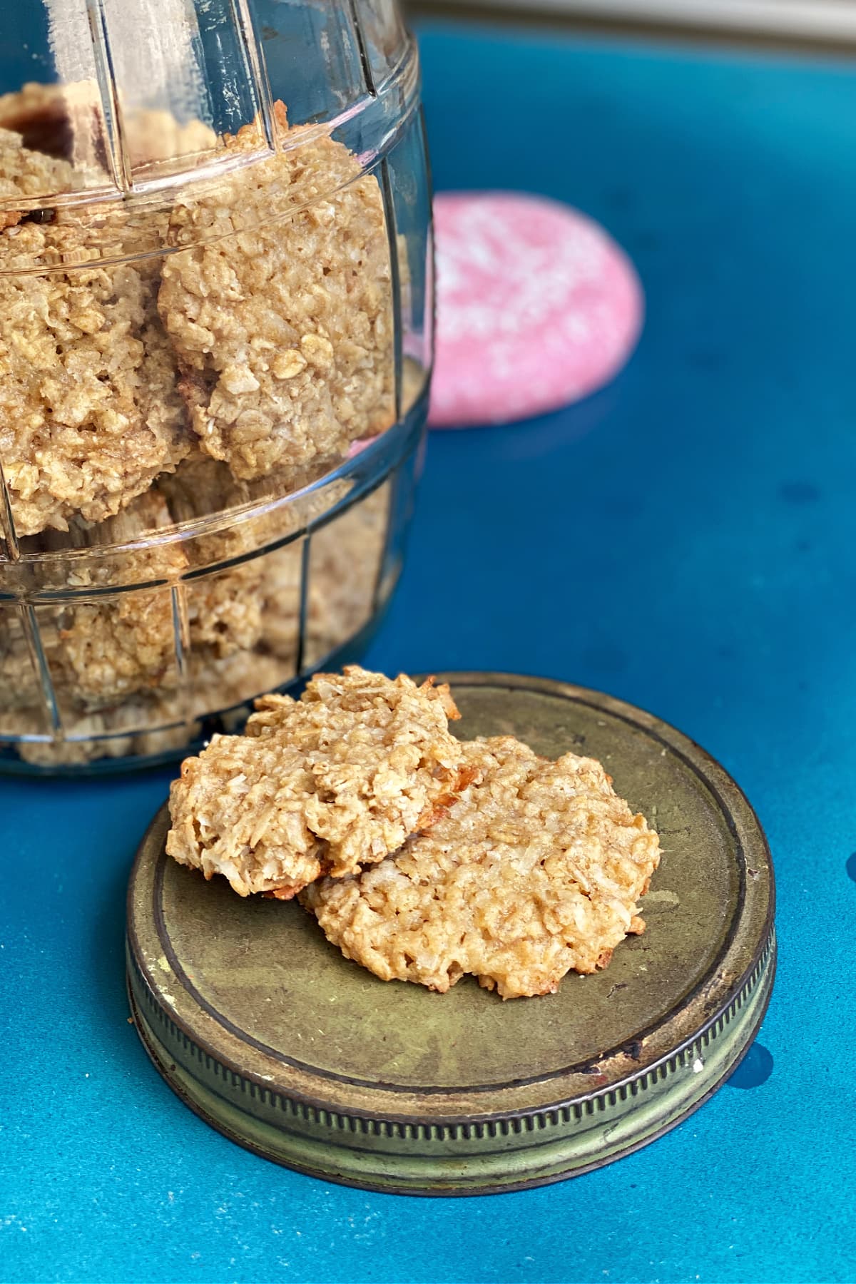 Coconut Oatmeal Cookies in an old pickle jar, with two cookies resting on the opened lid. 