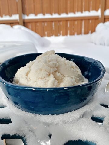 Snow ice cream in a bowl, setting on a snow-covered bistro table.