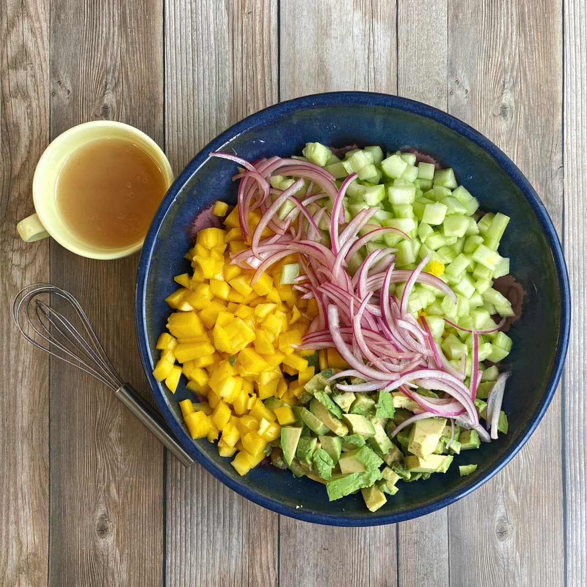 diced mango, cucumber, avocado, and sliced red onion in large blue bowl. 