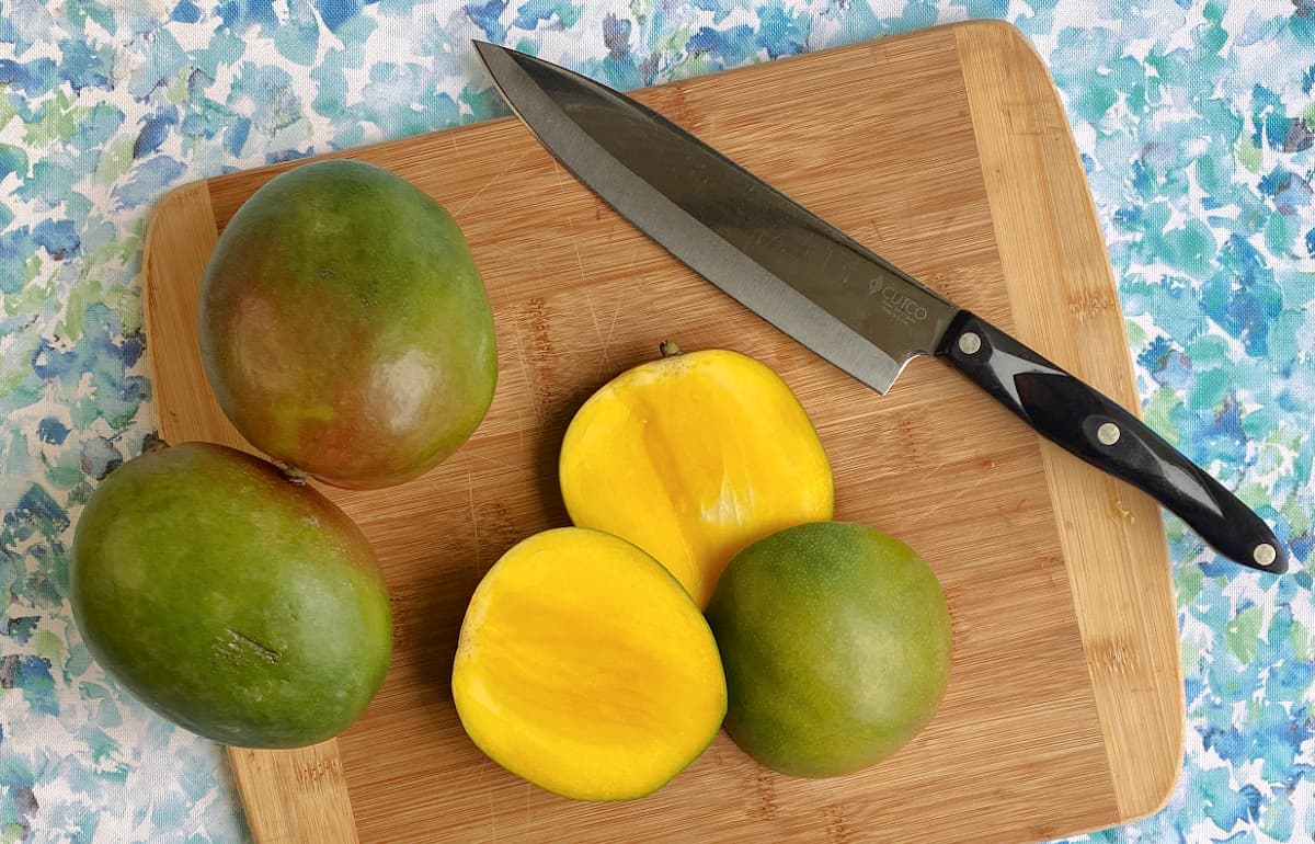 Cutting board with chef's knife and mangos cut and whole.