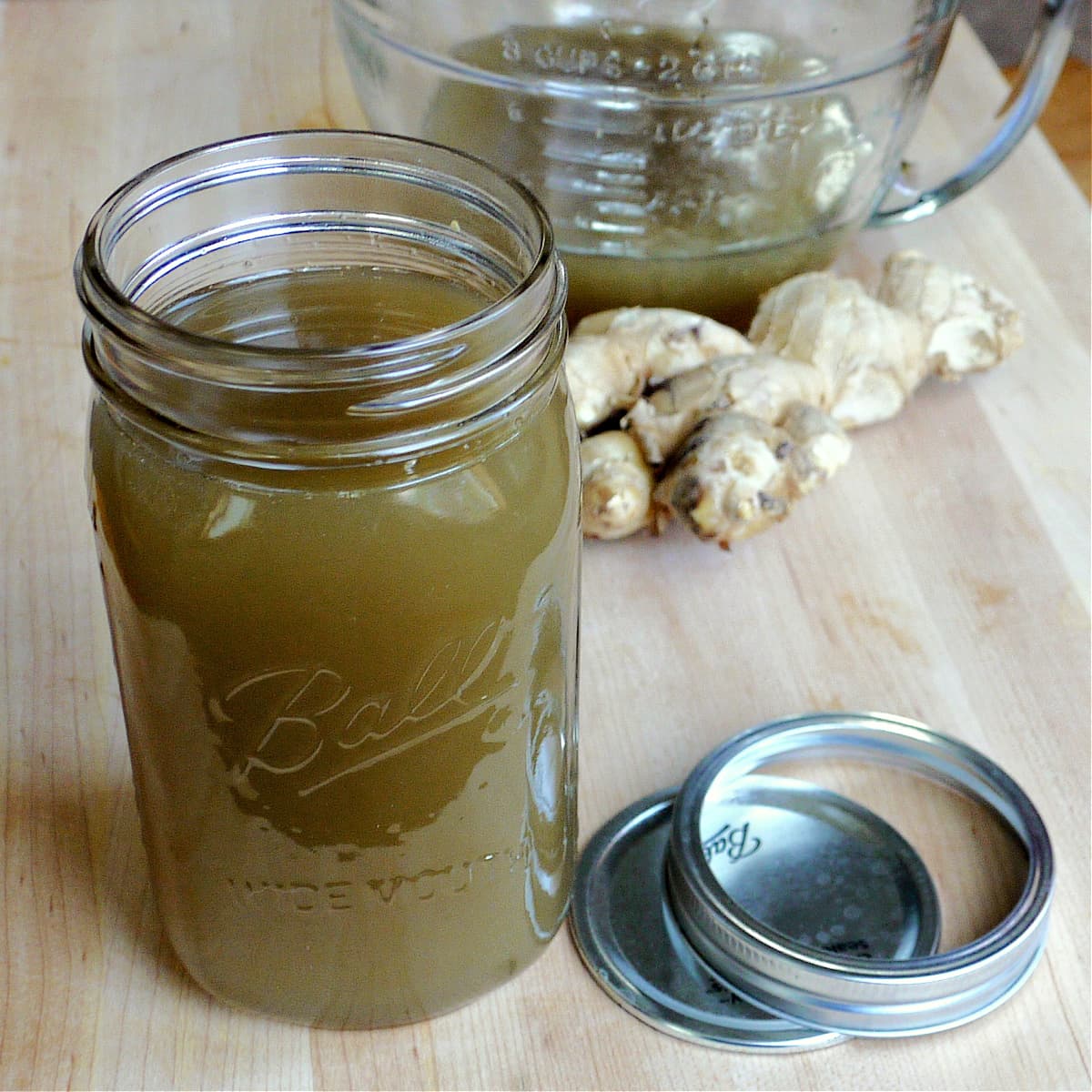 Mason jar filled with ginger syrup. Ginger root and more syrup in the background. 