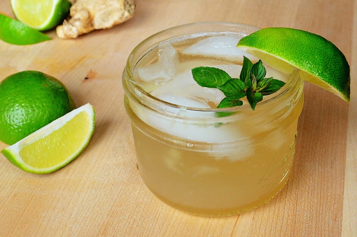 Close-up shot of Classic Whiskey Ginger with Lime is a short Mason jar, garnished with mint sprig and lime wedge.