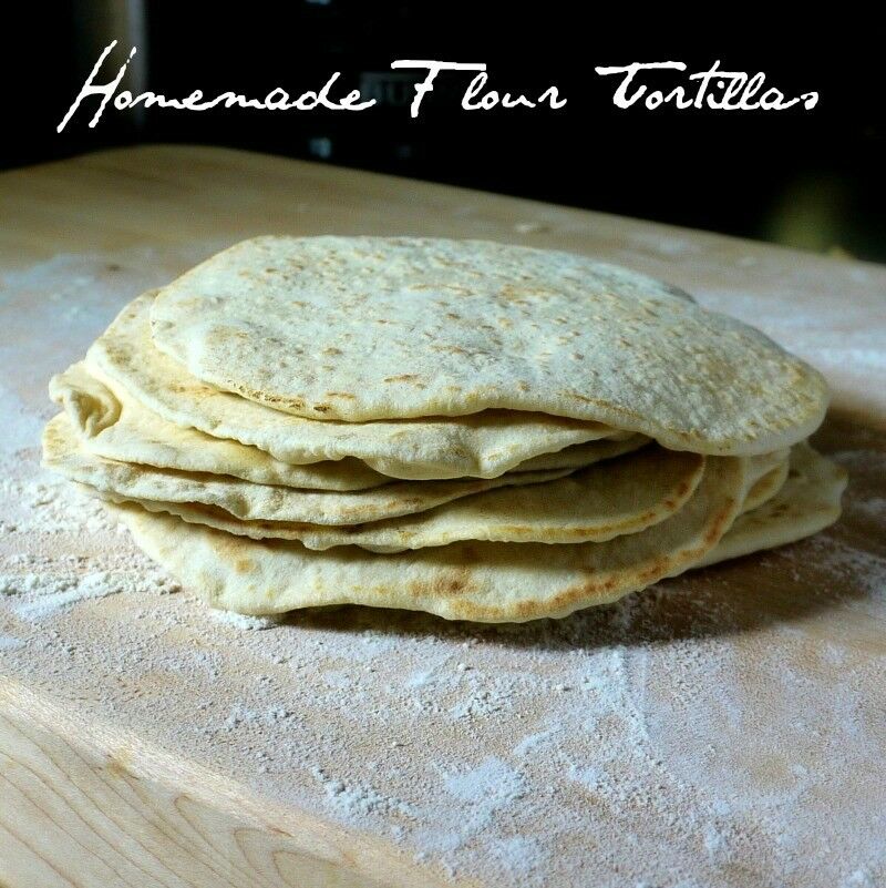 Stack of flour tortillas on a floured cutting board.