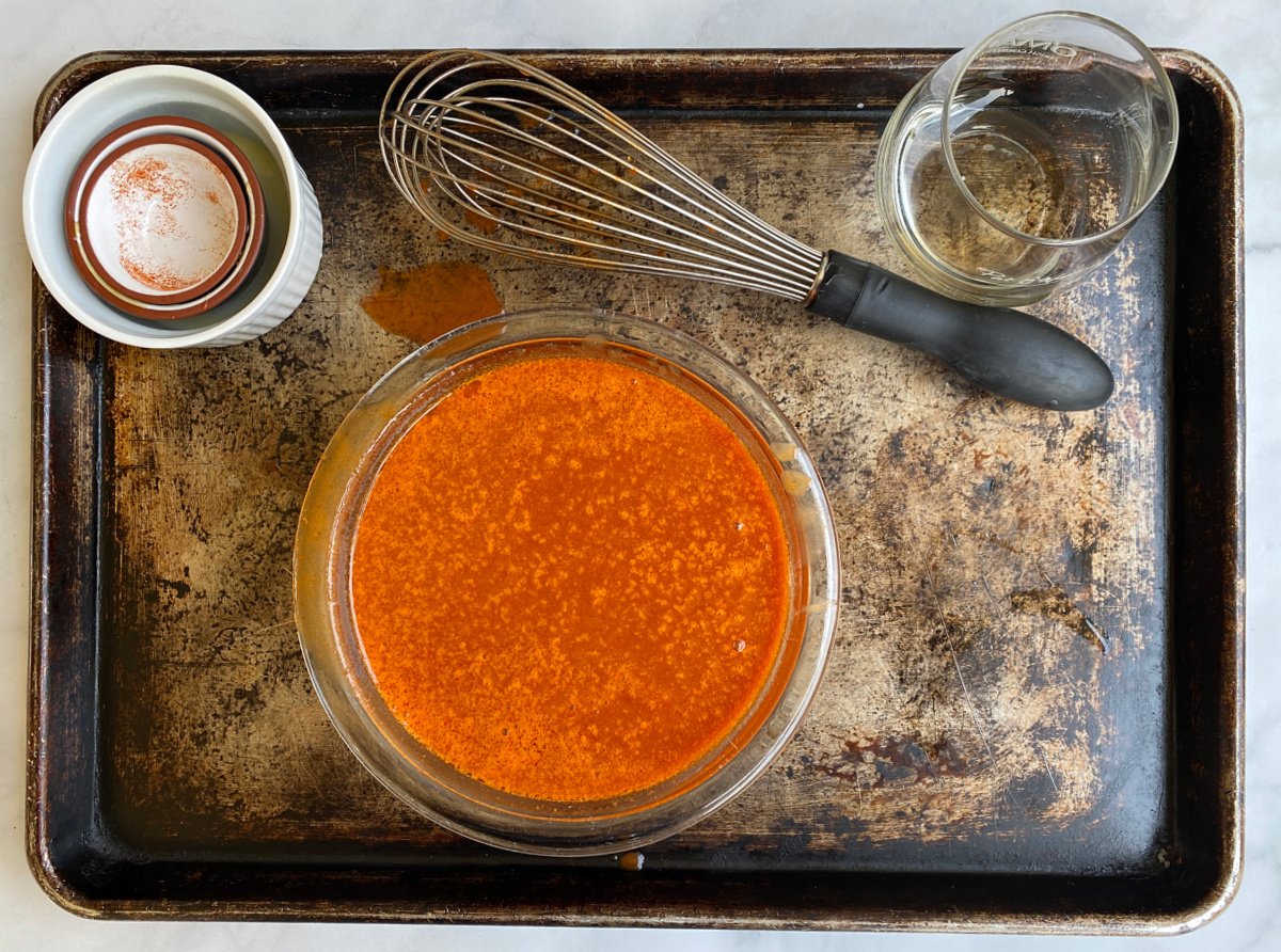 Wing Sauce mixed in a glass bowl, with small, empty ingredient bowls and wire whisk laying next to it. 