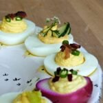 Close-up of deviled eggs with various garnishes, displayed on an egg plate.