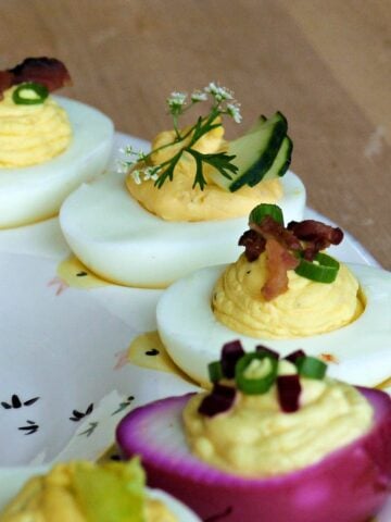 Close-up of deviled eggs with various garnishes, displayed on an egg plate.
