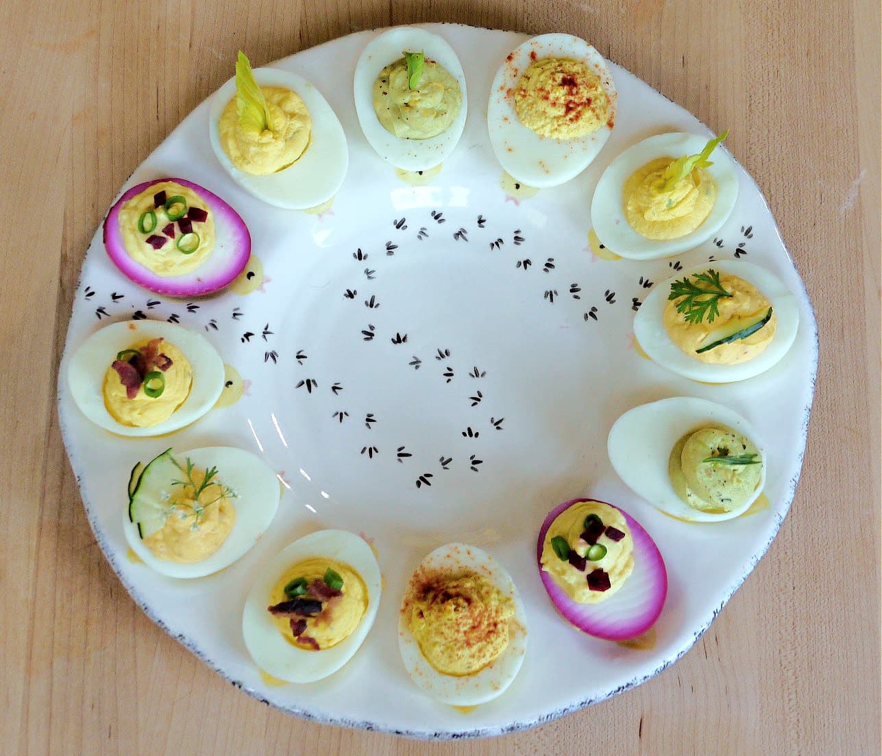 Overhead view of 12 deviled eggs with different types of garnishes, displayed on an egg plate.
