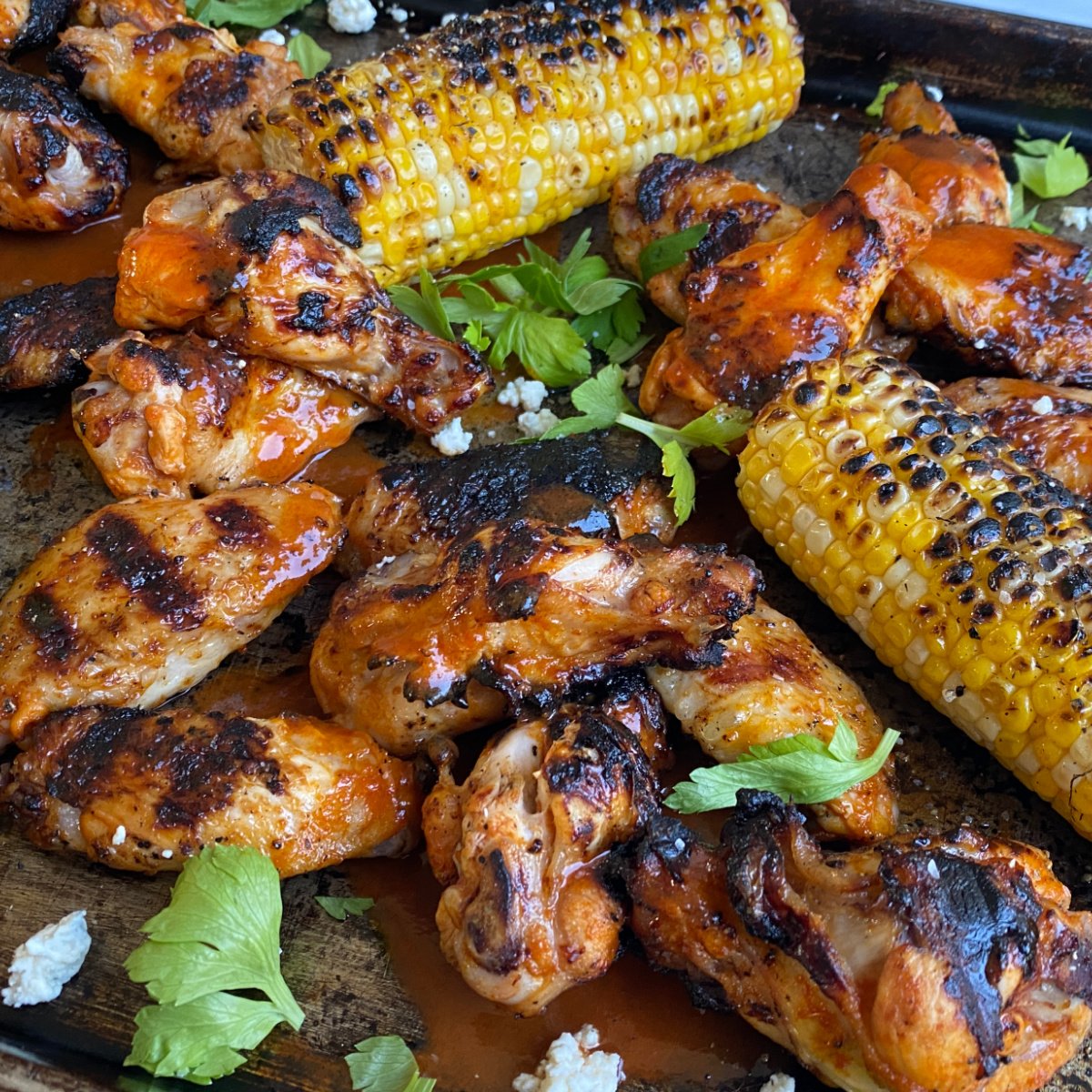 Grilled wings and grilled corn on old baking tray, garnished with cilantro and blue cheese. 
