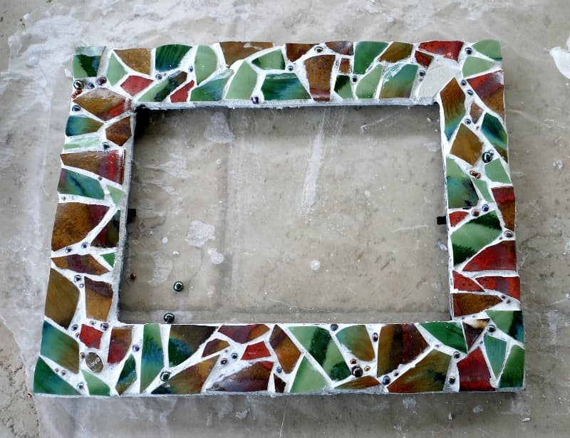 Broken pieces of pottery, tiles, plates, creating a mosaic on the face of a picture frame.