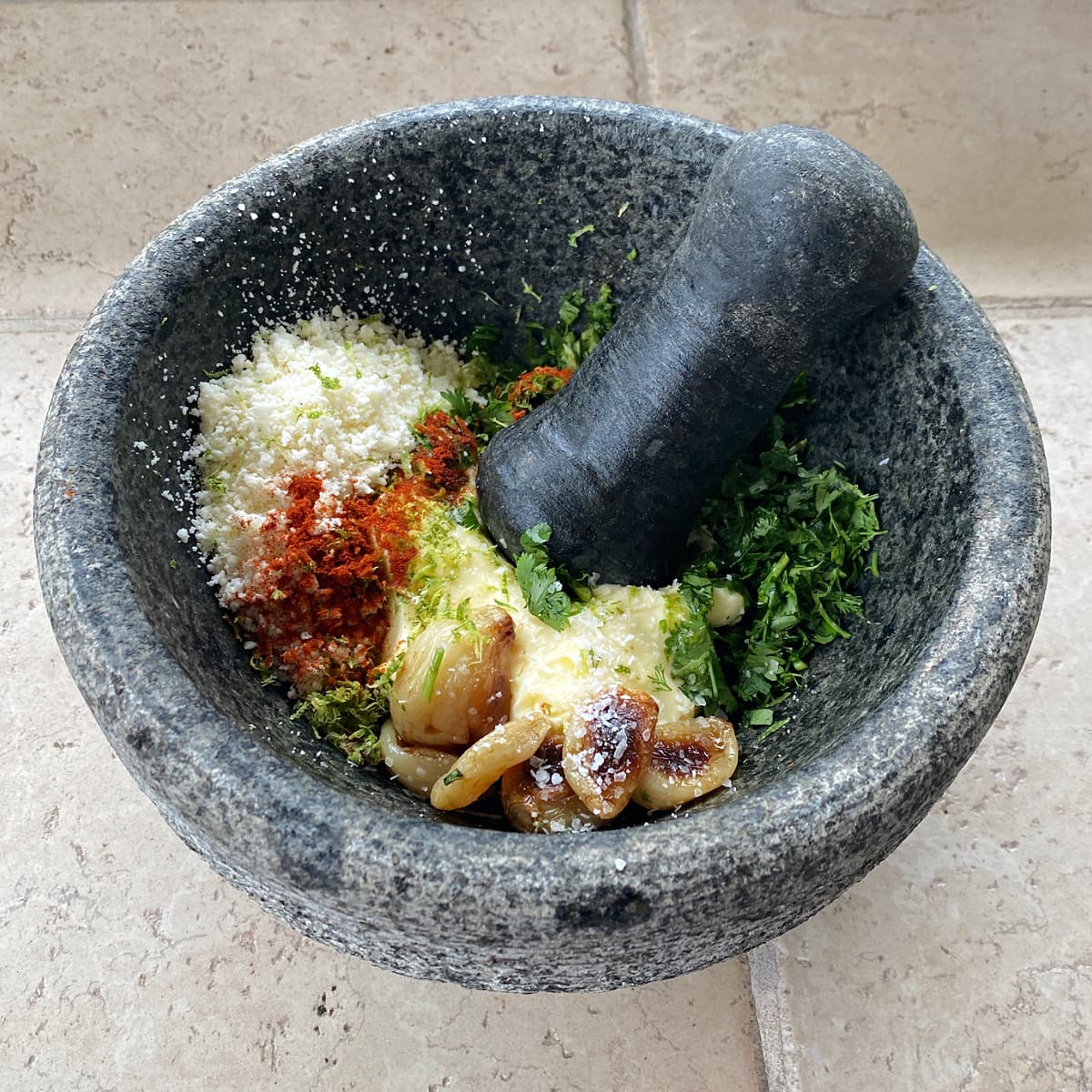 Elotes ingredients in molcajetes: cotija, roasted garlic, cilantro, butter, lime, and chipotle pepper. 