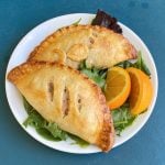 Two tuna hand pies on plate, garnished with orange slices.