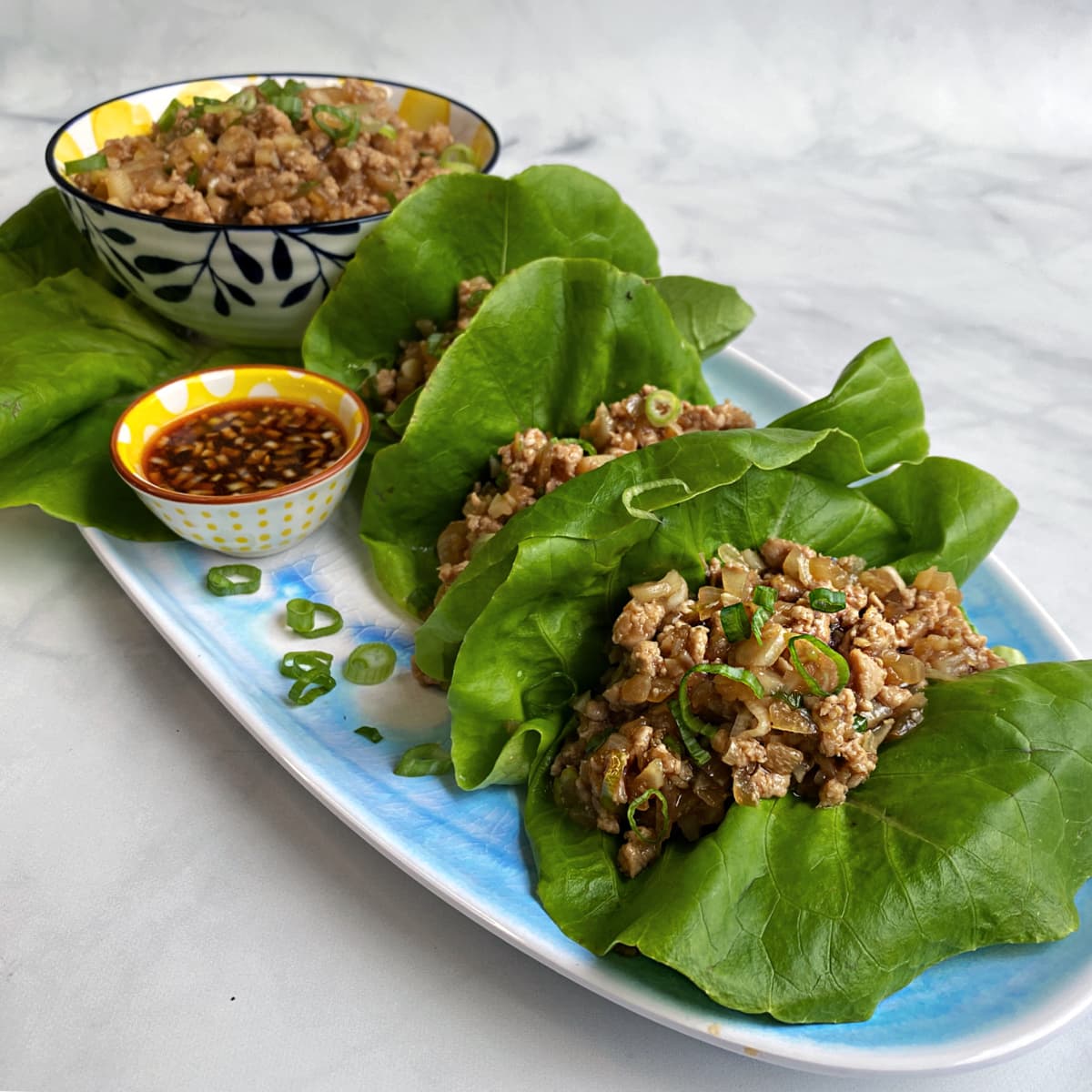 Chicken lettuce wraps on a long platter, with sauce and extra filling on the side.