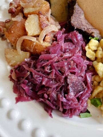 Geram red cabbage centered on a plate with German potato salad, sauerbraten, and spaetzle.