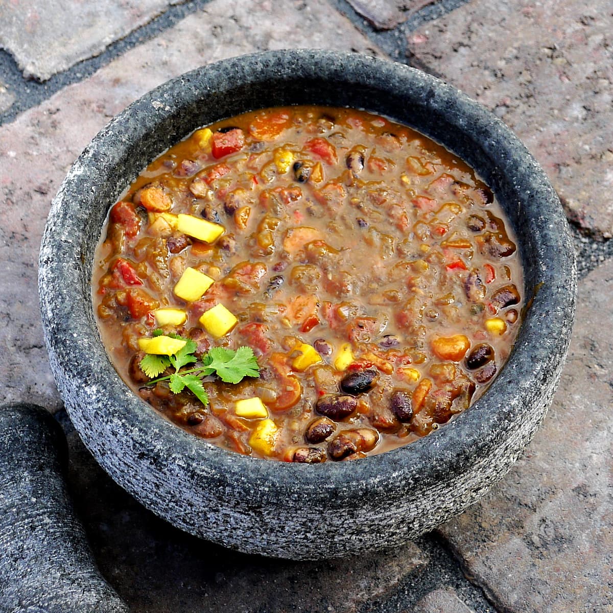 Chili in a stone bowl, garnished with diced mango and cilantro.