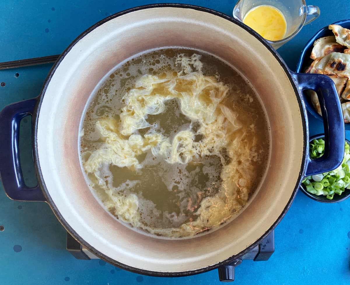 A thin ribbon of cooked eggs in chicken stock in Dutch oven. 