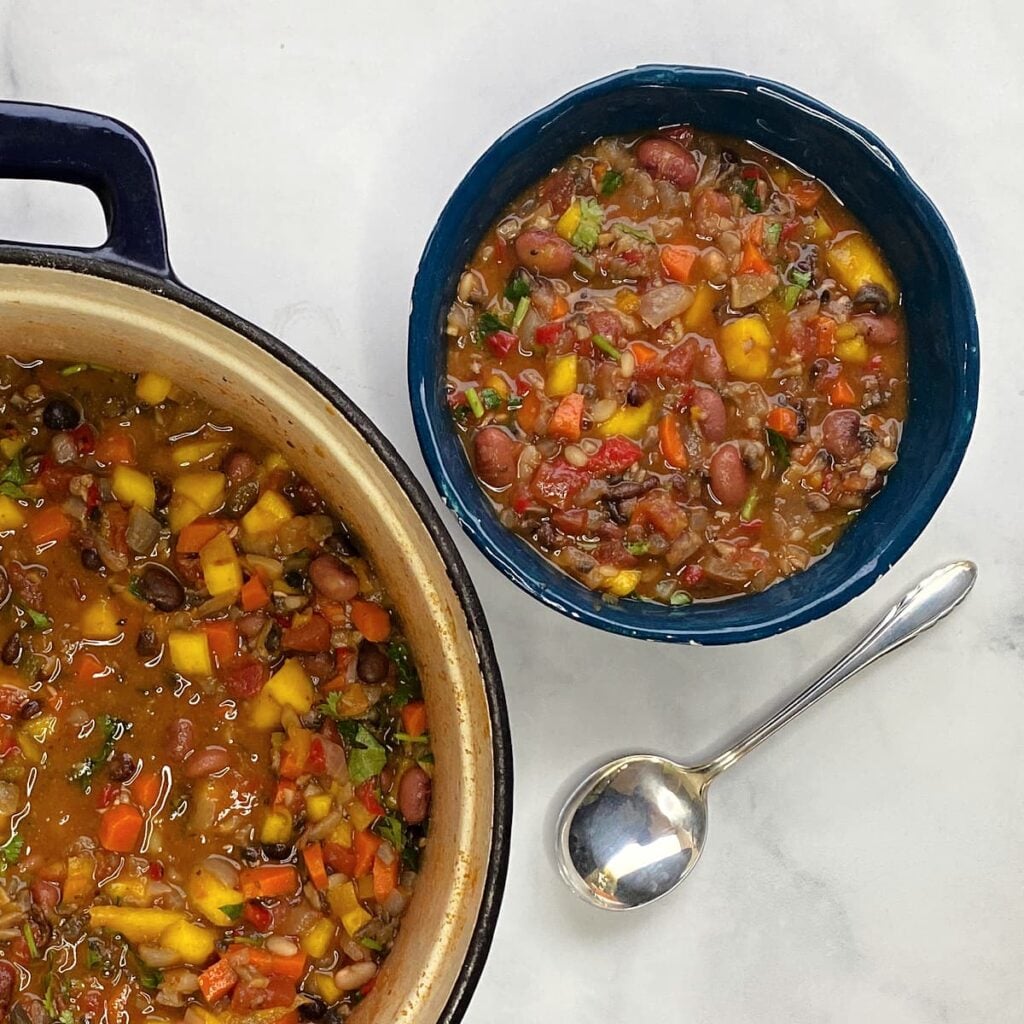 Bowl of mango chili with a spoon to the side. Corner of Dutch oven filled with cooked chili in view.